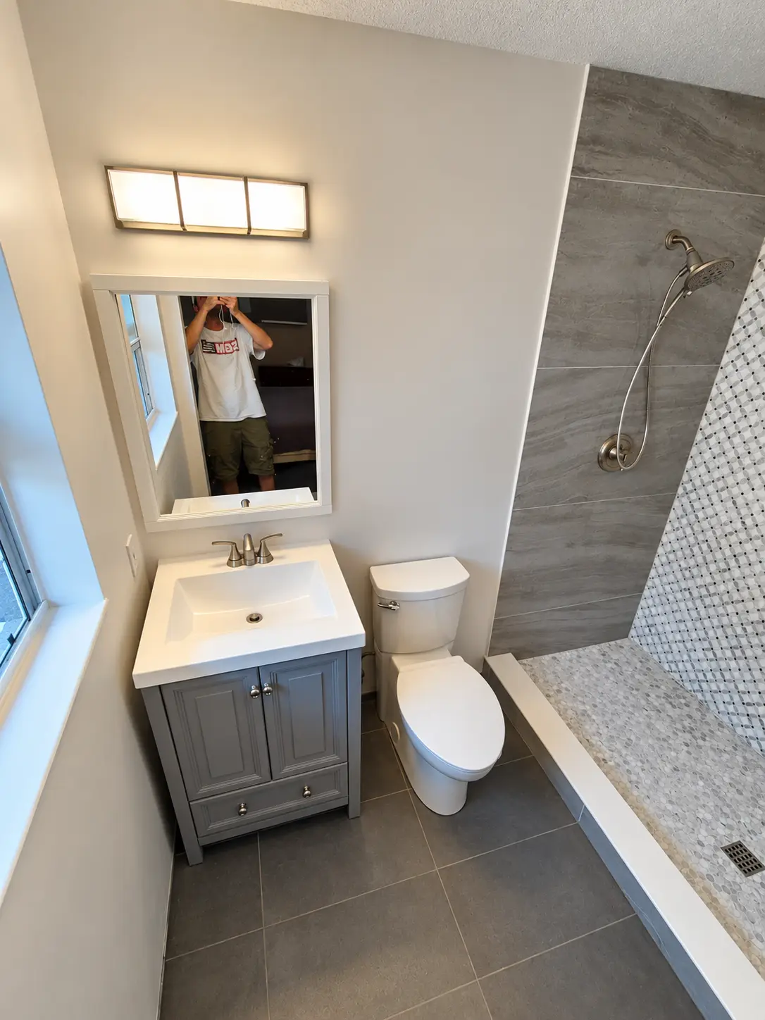 Gray tiled bathroom renovation with mosaic shower floor, gray vanity and brushed nickel fixtures
