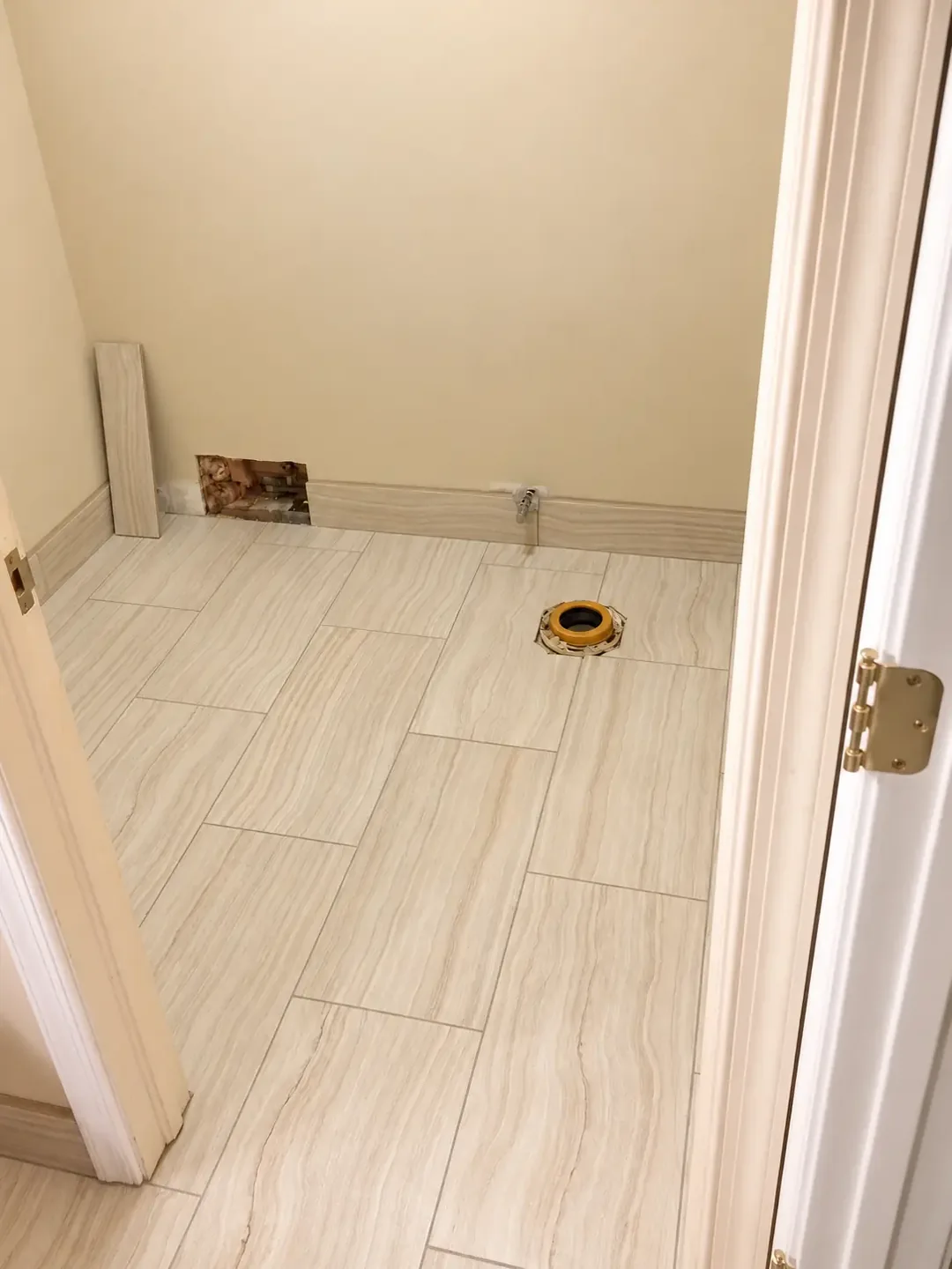 Beige wood-look bathroom floor tiles installed around a toilet plumbing opening during renovation