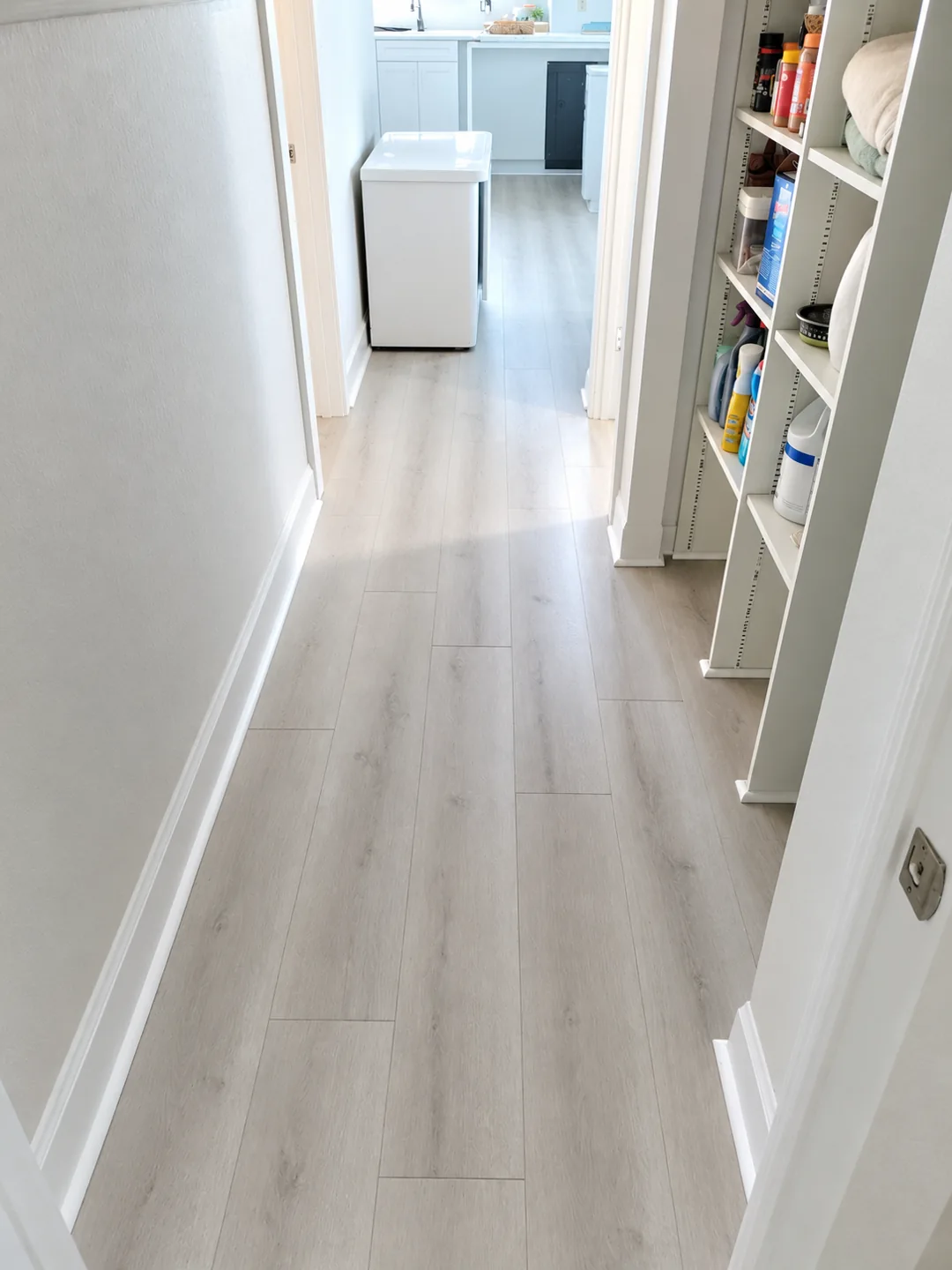 Light wood-look plank flooring continuing through a bright hallway into a laundry room