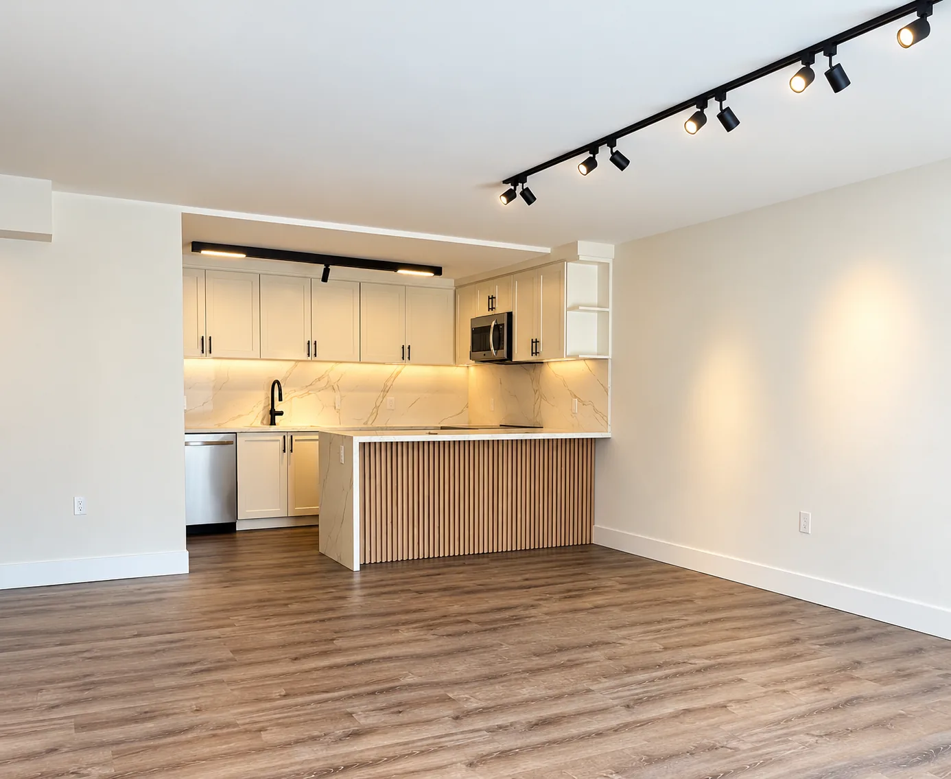 Open-plan kitchen with a fluted wood waterfall peninsula, marble-look backsplash, black track lighting, and wood-look flooring