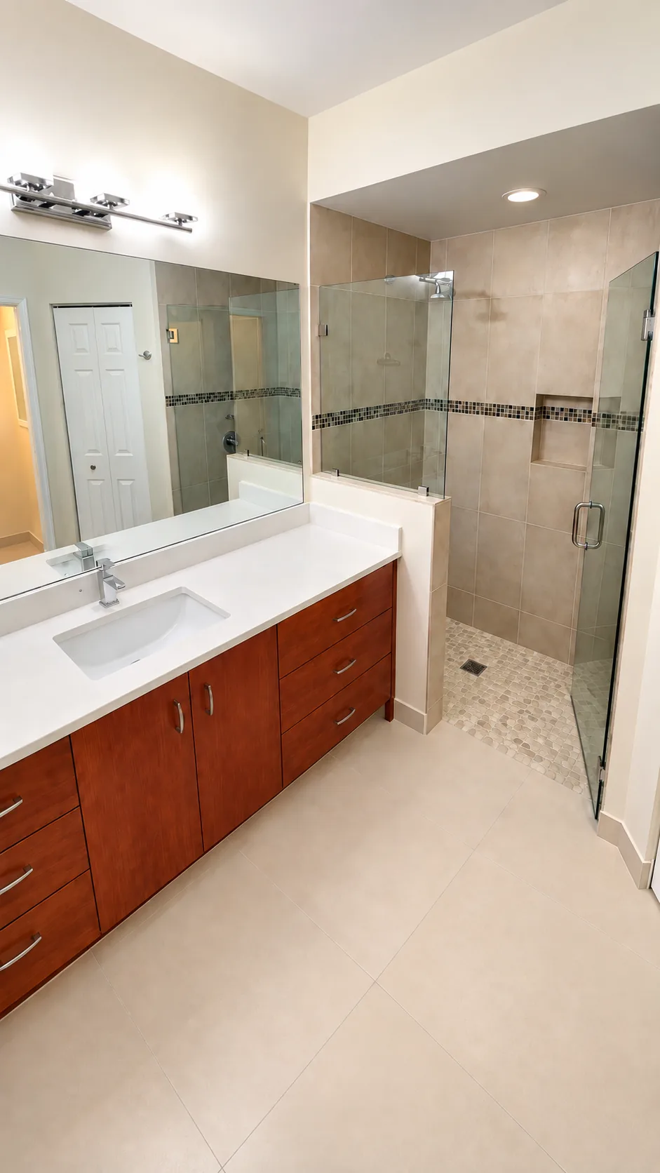 Bathroom remodel with wood vanity, white quartz counter and walk-in shower with pebble tile floor and mosaic accent band