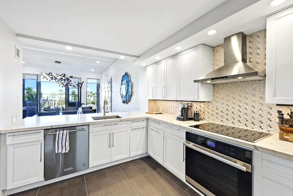 Bright white shaker kitchen with a marble-look countertop island, mosaic tile backsplash, and water views