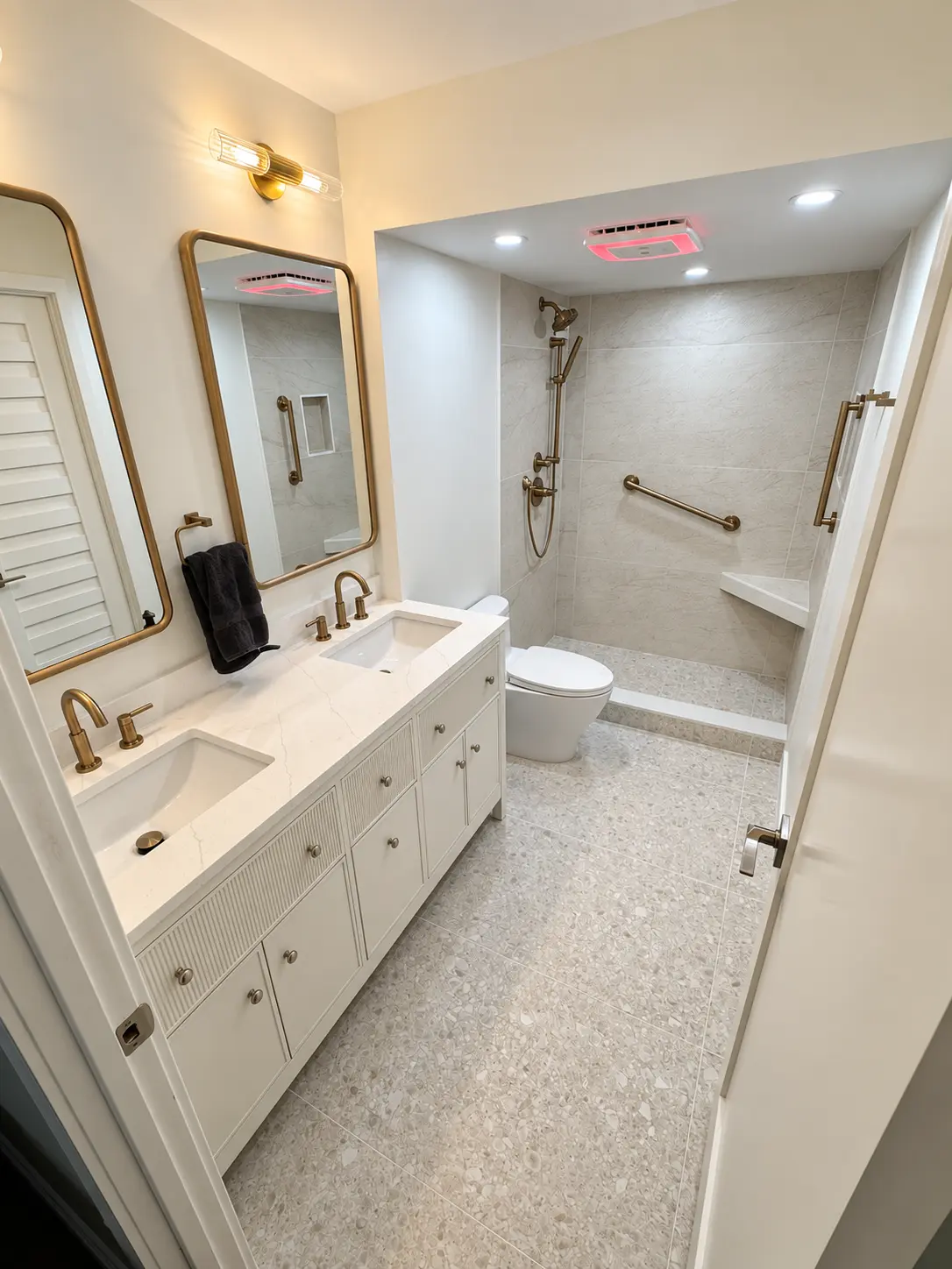 Spa-style bathroom with brushed brass fixtures, double vanity, grab bars and curbless accessible shower with bench