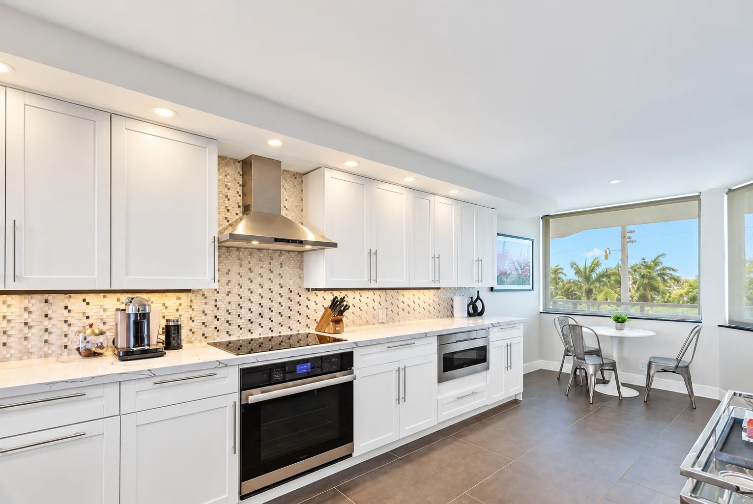 White shaker kitchen with a mosaic tile backsplash, stainless appliances, and a window-side dining nook