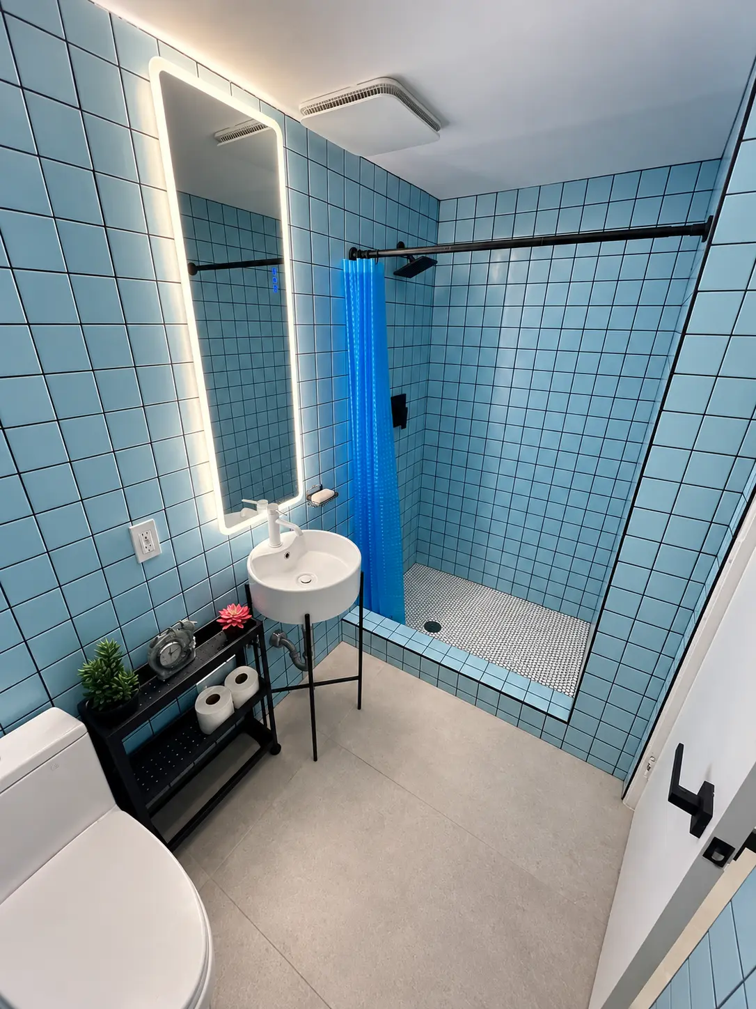 Aqua tiled bathroom with walk-in shower, penny tile floor and lit mirror