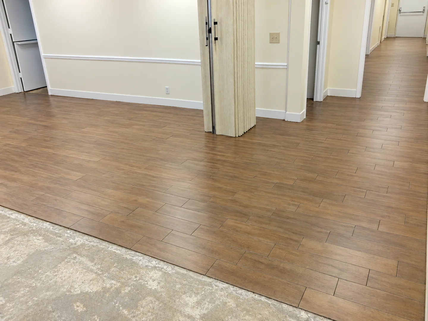Warm brown wood-look flooring in a renovated interior with white trim and connected hallway